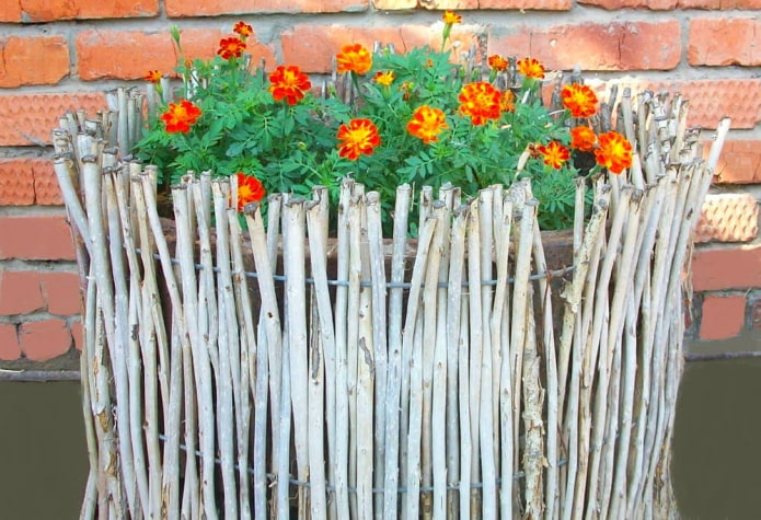 decoration of the sides of the flower bed with thin branches, vertically inserted into the wire frame